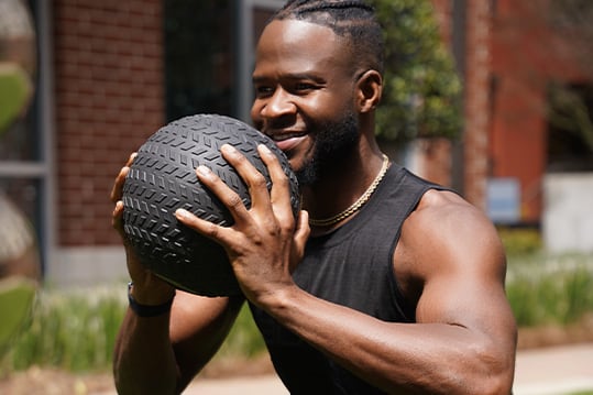 Coach is smiling and holding a black ball to his chest